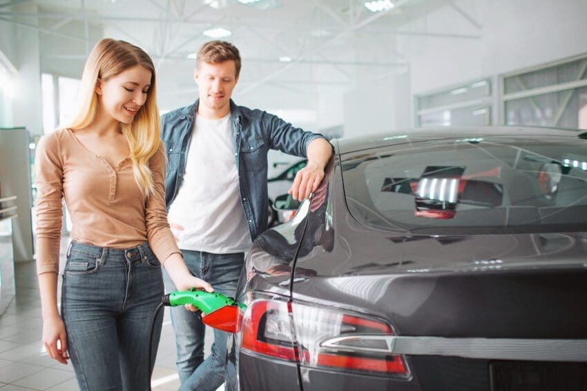 Young,Couple,Buying,First,Electric,Car,In,The,Showroom.,Woman